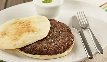 Prato com kafta, um potinho com molho e talheres ao lado